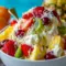 A bowl of Hawaiian Cheesecake Salad with pineapple, strawberries, kiwi, raspberries, and toasted coconut in a creamy cheesecake filling.