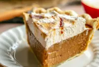 Slice of apple butter pie with cinnamon whipped cream on a white plate, showing flaky butter crust and a silky, custard-like filling, Apple Butter Apple Pie.