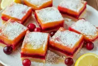 Close-up of golden Christmas Lemon Bars with layers of tart cranberry and lemon custard dusted with powdered sugar – the ultimate Baking With Fresh Cranberries dessert for the holidays.