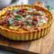 Caramelized Onion Tart with Pumpkin, Ricotta, Bacon & Sage — Thanksgiving Recipes & Fall Cooking Golden puff-pastry tart topped with browned sweet onions, dollops of pumpkin-ricotta, crisp bacon bits, and scattered sage leaves on a wooden board.