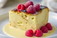 Golden-brown bread pudding slices topped with vanilla sauce and fresh berries on a white plate.