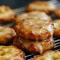 Golden baked apple fritters dotted with apple pieces, drizzled with vanilla glaze and dusted with cinnamon, arranged on a parchment-lined baking sheet.