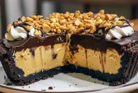 Close-up of a no-bake peanut butter pie with glossy chocolate ganache, Oreo crust, and crushed candy and peanuts on top.