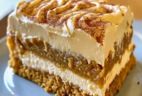 Close-up of a slice of gooey pumpkin cake drizzled with brown sugar cream cheese frosting, showing a custardy center, smooth frosting, and a sprinkle of chopped pecans and cinnamon.