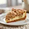 Slice of Snickerdoodle cream cheese apple pie with crumb topping and caramel drizzle on a white plate.