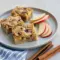 Thanksgiving Apple Brownies — Easy Thanksgiving Apple Recipes Square apple blondie bars studded with apple pieces and pecans on a wooden board, one piece topped with a scoop of vanilla ice cream.