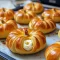 Golden crescent rolls shaped like pumpkins, filled with creamy pumpkin and cream cheese, dusted with cinnamon and arranged on a wooden serving board.