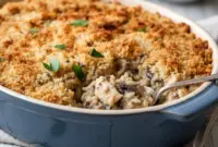 Golden, cheesy Baked Chicken Wild Rice Casserole in a white baking dish, topped with crispy panko breadcrumbs and garnished with fresh herbs.