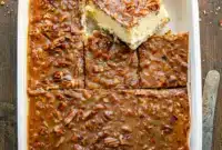 A rich Cheesecake With Pecan Pie Topping featuring a buttery crust, creamy cheesecake layer, and glossy caramelized pecans drizzled over the top — the ultimate Baking With Pecans dessert.