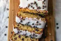 Sliced Chocolate Chip Cookie Bread Loaf on a cooling rack with chocolate chips sprinkled on top, golden edges, tender cookie-like crumb, and a drizzle of glaze across the surface.