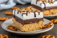 A decadent Chocolate Peanut Butter Bliss Cheesecake with a crunchy pretzel crust, creamy peanut butter cheesecake filling, smooth chocolate layer, and drizzled chocolate sauce, topped with whipped cream and crushed pretzels.