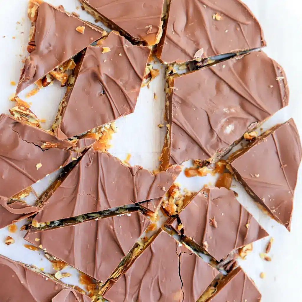 Close-up of broken toffee with toasted pecans and glossy chocolate, a sweet snack trending among Trending Desserts 2025, inspired by a light Sponge Toffee Recipe texture.