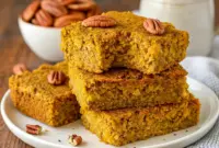 Gluten Free Pumpkin Oatmeal Bars – Easy, Filling & Packed with Fall Flavor1 A stack of chewy Gluten Free Pumpkin Oatmeal Bars drizzled with maple syrup and sprinkled with oats — a cozy fall breakfast treat that’s healthy, filling, and bursting with pumpkin spice flavor.