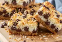 Heavenly Coconut Chocolate Bars with Graham Cracker Crust – Sweet & Savory Dreams1 Golden coconut chocolate bars with a buttery graham cracker base, glossy chocolate layers, and lightly toasted coconut topping cooling on a rustic baking tray.