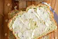 Honey And Oat Bread – Simple, Sweet, and Totally Foolproof Comfort Bake1 Freshly baked Honey And Oat Bread loaf topped with golden oats, sliced on a wooden board beside a drizzle of honey and melting butter.