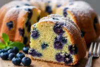 Golden blueberry bundt cake sliced and served on a rustic plate, ideal for a joyful morning treat or brunch table centerpiece.
