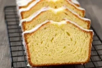 A sliced loaf of Glazed Eggnog Bread on a white platter with a thick eggnog drizzle and sprinkled nutmeg on top, showing a soft and moist texture, festive and cozy holiday baking scene.