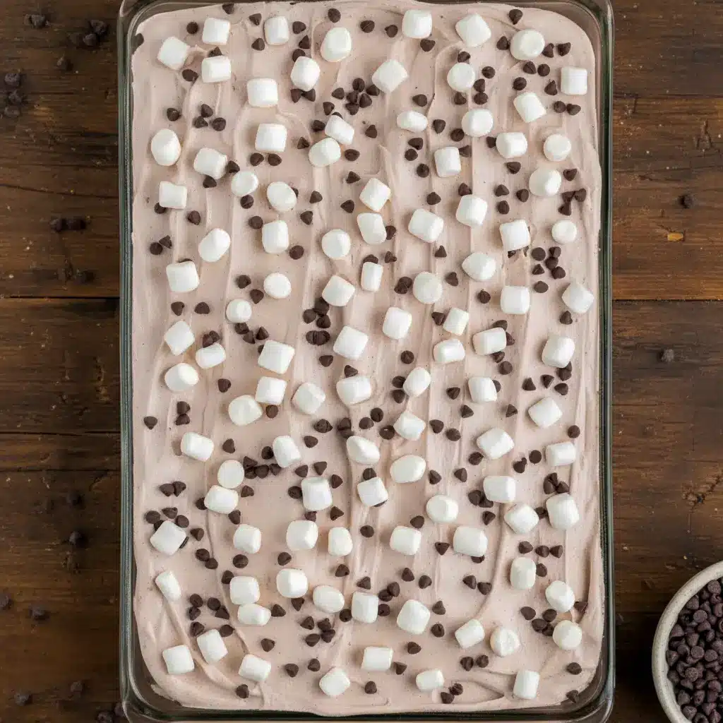 Rich hot cocoa poke cake topped with fluffy whipped chocolate frosting, melted marshmallows, and chocolate chips, served on a festive holiday dessert table.