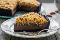 Pure Indulgence German Chocolate Pies with Toasted Coconut & Pecans1 Slice of rich no-bake German chocolate pie with creamy chocolate filling, toasted coconut-pecan topping, and a dark Oreo cookie crust on a plate.