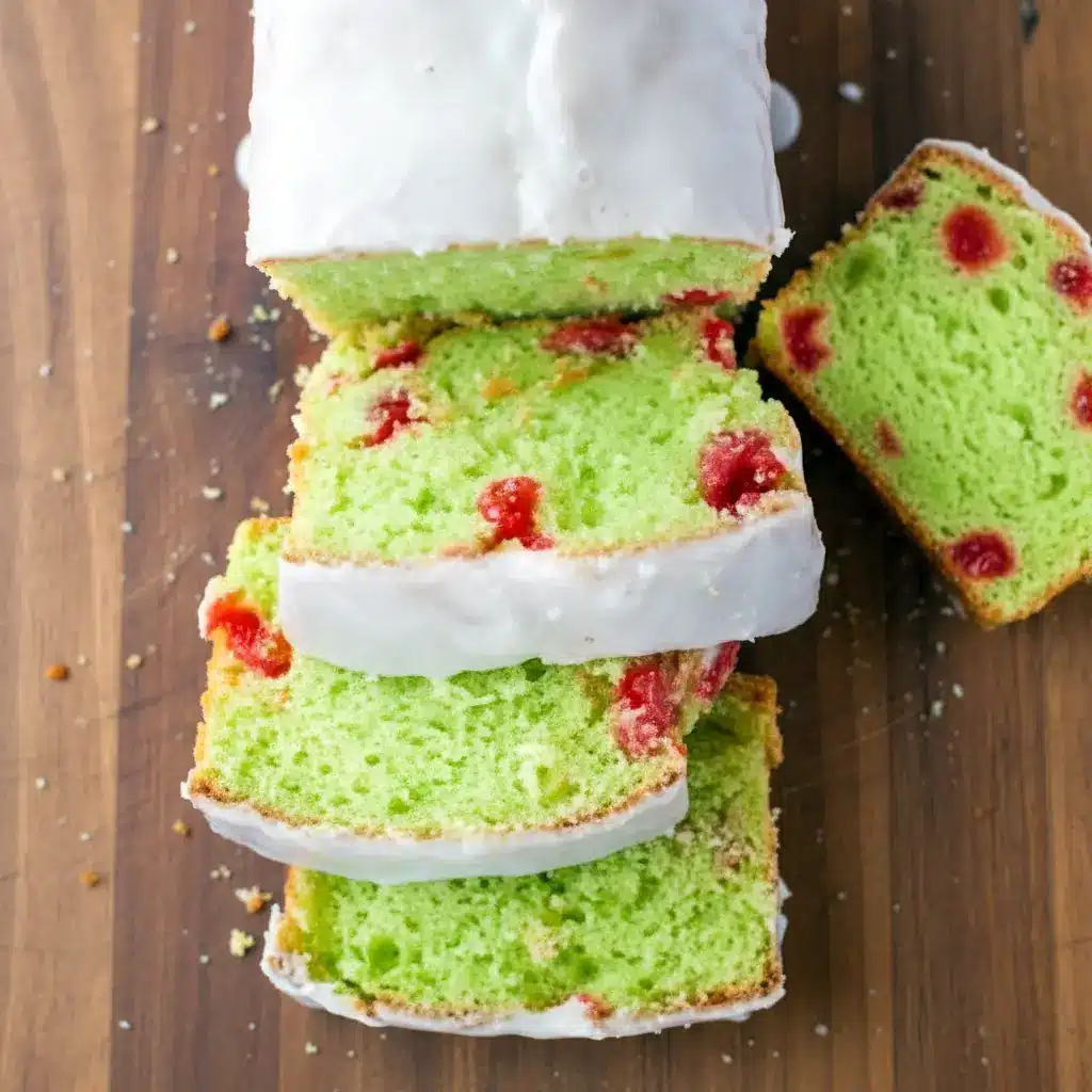 Moist pistachio loaf studded with maraschino cherries, drizzled in glossy almond glaze and styled for a warm holiday dessert table.