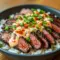 Addictive Korean BBQ steak and rice bowl featuring juicy sliced steak, fluffy rice, fresh vegetables, and a creamy spicy sauce for a bold, flavorful dinner.