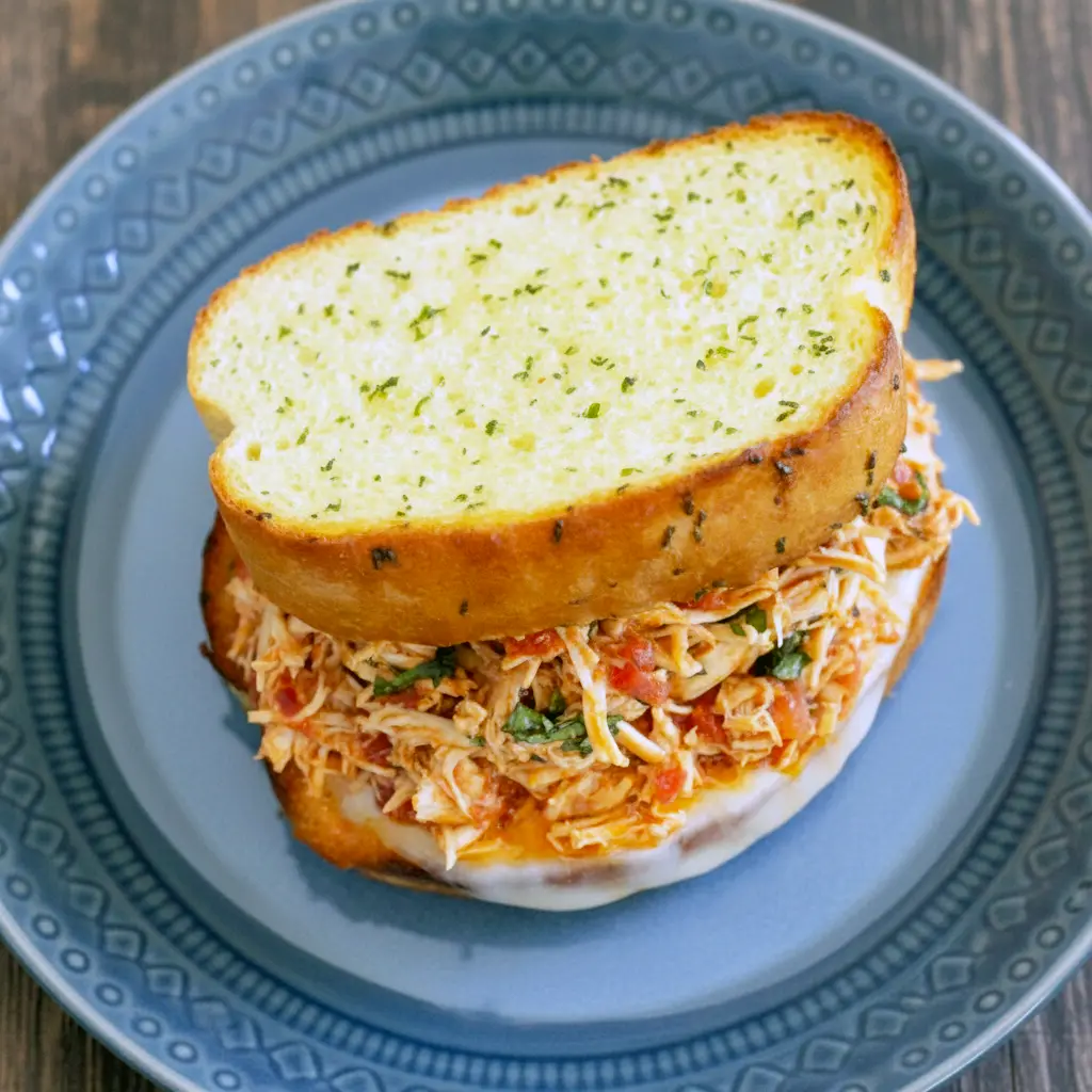 Close-up of warm garlic-bread Italian Chicken Sandwiches stacked with tender Shredded Italian Chicken, melted provolone, fresh basil, and rich tomato-herb sauce.