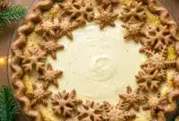 Irresistible Eggnog Pie with Gingerbread Crust – A Festive Eggnog Dessert Dream2 Slice of creamy ginger-spiced Eggnog Pie With Gingerbread Crust topped with whipped cream and nutmeg, served on a holiday table with festive decorations.