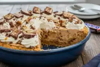 Close-up of a creamy no-bake Snickers pie topped with chopped candy bars, showing its layered texture and rich chocolate-peanut-caramel swirl.