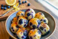 Powerful Lemon Blueberry Cottage Cheese Protein Bites – One of the Best Nutritional Foods3 Lemon blueberry cottage cheese protein bites arranged on parchment with fresh blueberries and lemon zest for a healthy snack.