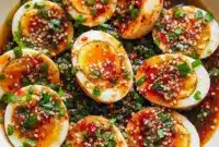 Spicy Chili Garlic Deviled Eggs You’ll Crave – Easy Boiled Eggs Meal Ideas1 Plate of spicy chili garlic deviled eggs topped with crunchy chili crisp, sesame seeds, and herbs, arranged for a flavorful starter or snack.