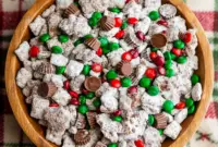 Bowl of sweet and crunchy holiday Reindeer Food Puppy Chow coated in powdered sugar with festive candies, perfect for Christmas snacking and winter dessert parties.
