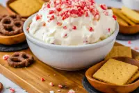 A bowl of creamy peppermint dessert dip topped with crushed candy pieces, styled for the holidays and served with chocolate cookies and pretzels, inspired by Jalapeno Popper Dip, Peppermint Cheesecake, classic Cheesecake Dip, and fun party favorites like Taco Dip.