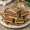 A glossy sheet of chocolate-covered Saltine Toffee topped with Toasted Almonds, broken into pieces and arranged on a holiday Dessert Tray, surrounded by festive Christmas Table Decorations—a perfect sweet addition for Hosting Christmas Dinner and completing any Christmas Dessert Table.