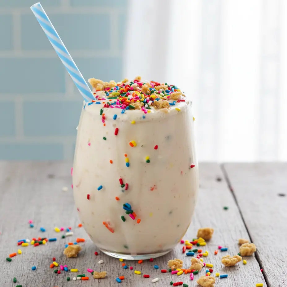 A tall, creamy blender-made drink showcasing classic Birthday Cake Protein Shake Ingredients, topped with sprinkles and granola, perfect for fans of Birthday Cake Protein Shake Recipes, indulgent Cake Batter Protein Shake Recipes, and a thick, dreamy Cake Batter Protein Shake served cold.