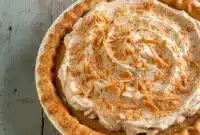A slice of bourbon butterscotch pie topped with Butterscotch Whipped Cream and fluffy Molasses Whipped Cream, featuring a golden filling in a crisp Bourbon Pie Crust, styled as an elegant holiday dessert.
