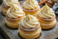 Golden cream puffs dusted with powdered sugar and filled with spiced eggnog cream, showcasing indulgent Cream Puff Fillings as a stunning Puff Pastry Holiday Dessert. A beautiful addition to Winter Sweet Treats, cozy Dessert Recipes Winter, and crowd-pleasing Christmas Potluck Dessert Ideas for holiday gatherings.