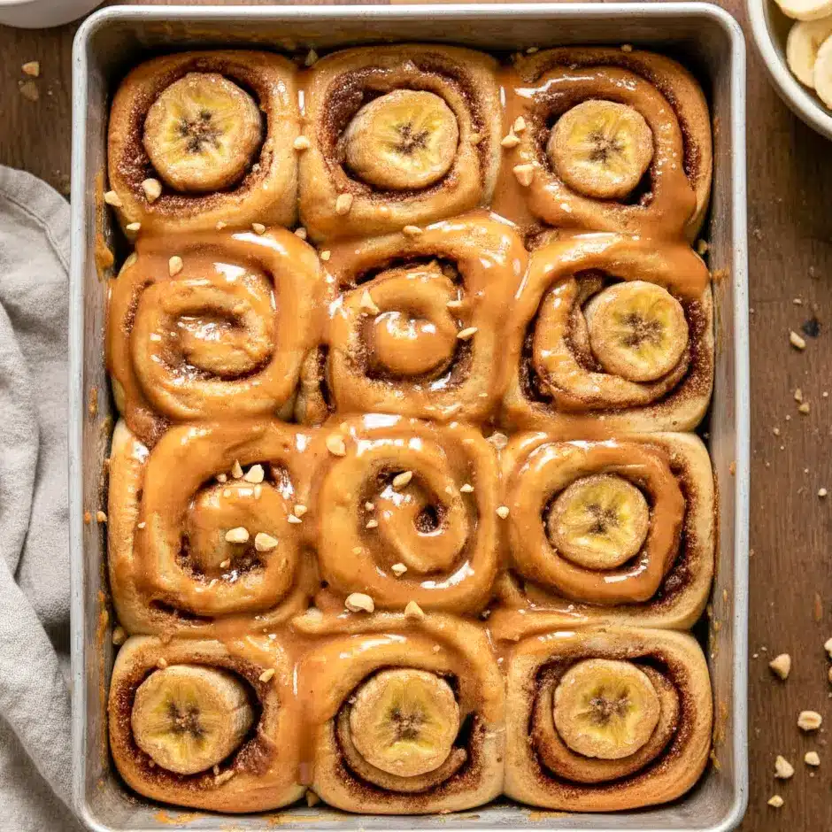 Freshly baked cinnamon rolls topped with peanut butter glaze, styled as Vegan Peanut Butter Banana Cinnamon Rolls, served warm and golden. A homemade alternative to Boxed Cinnamon Rolls, showcasing a soft Peanut Butter Pastry with banana slices, perfect for learning How To Make Peanut Butter Cinnamon Rolls at home.