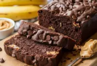 Thick slices of Chocolate Peanut Butter Banana Loaf with visible chocolate chips and peanut butter swirls, showcasing a moist crumb and rich cocoa color—an irresistible Banana Bread With Peanut Butter And Cocoa fresh from the loaf pan.