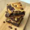 Stacked squares of Almond Flour Brownies No Sugar layered into a decadent Gluten Free Brookie, showing chewy cookie swirls over fudgy brownie layers with melty chocolate chips on top.