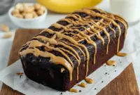 Freshly sliced Banana Bread Recipe Broma style loaf loaded with peanut butter and chocolate chunks, showing a moist crumb and glossy topping for a rich, dessert-like banana bread presentation.