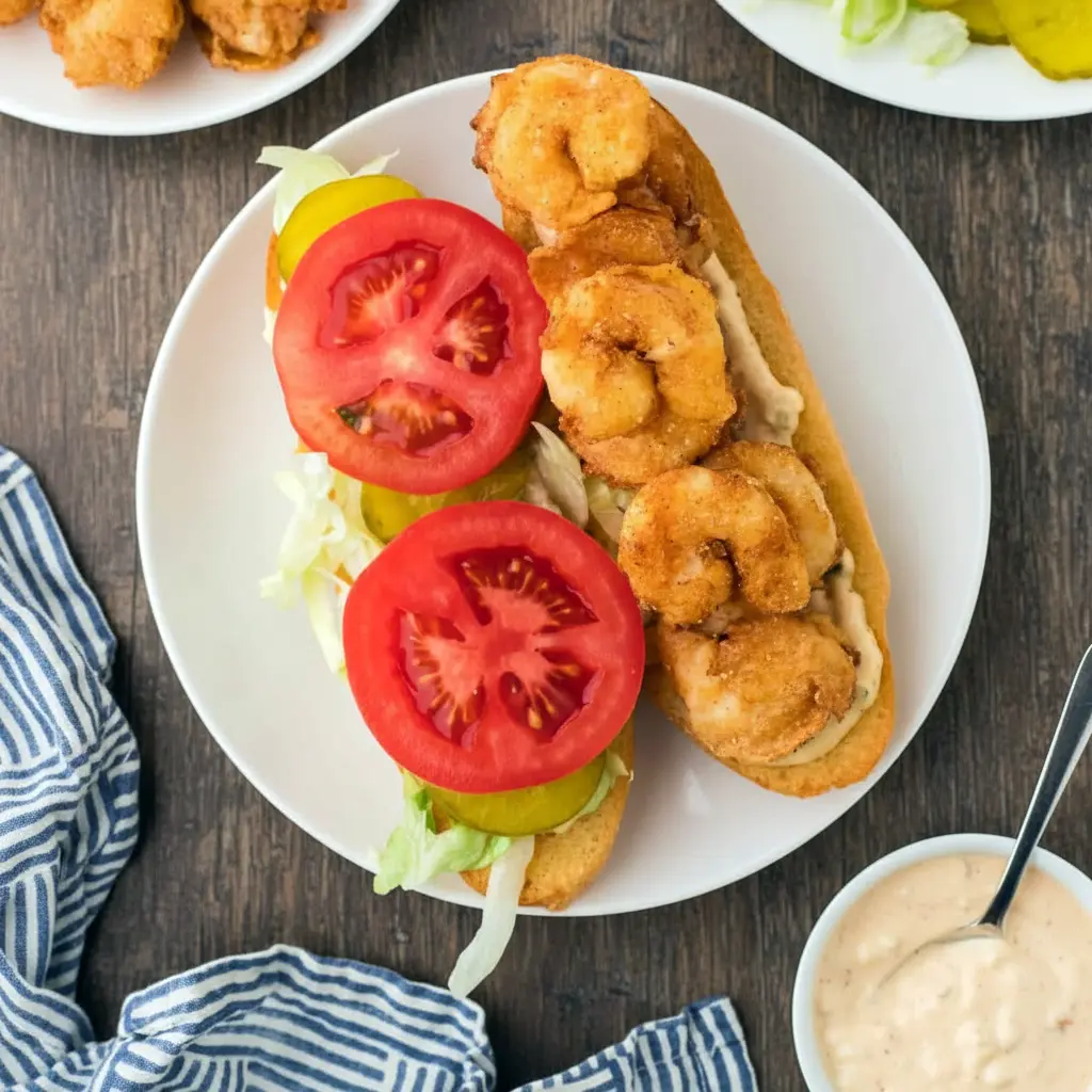 Shrimp Poboys Recipe featuring a crispy Fried Shrimp Sandwich stacked on French bread with lettuce, tomatoes, pickles, and rich Creole Sauce For Po Boy, inspired by iconic New Orleans flavors.