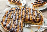Slice of Samoas Cookie Pie topped with toasted coconut, caramel drizzle, and melted chocolate, inspired by Samoas Cookies Recipe and classic Girl Scout Cookie Recipes, served as a rich and gooey Samoa Pie dessert.