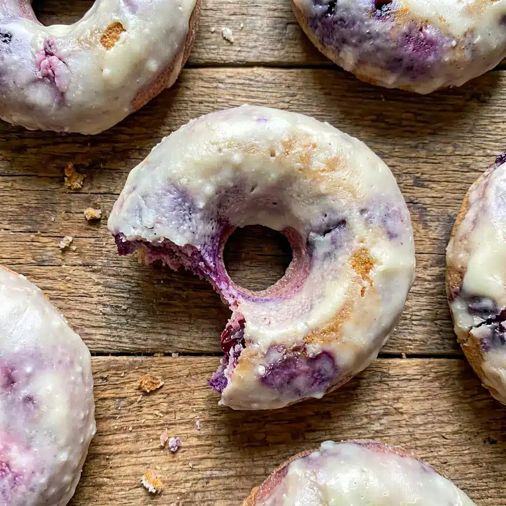 Freshly glazed Blueberry Cake Donuts stacked on a cooling rack with juicy blueberries, perfect for a High Protein Donut Recipe and healthy breakfast treat.