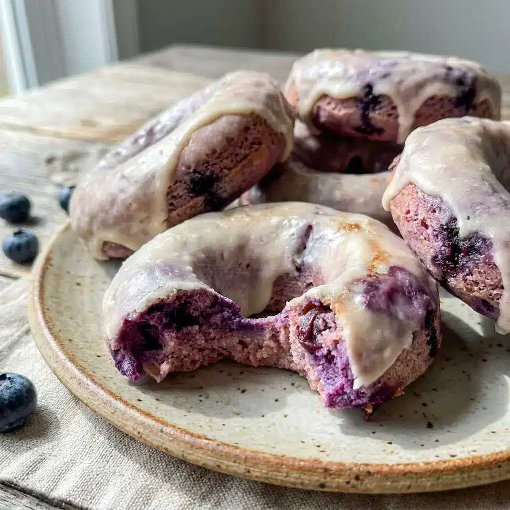 Freshly glazed Blueberry Cake Donuts stacked on a cooling rack with juicy blueberries, perfect for a High Protein Donut Recipe and healthy breakfast treat.