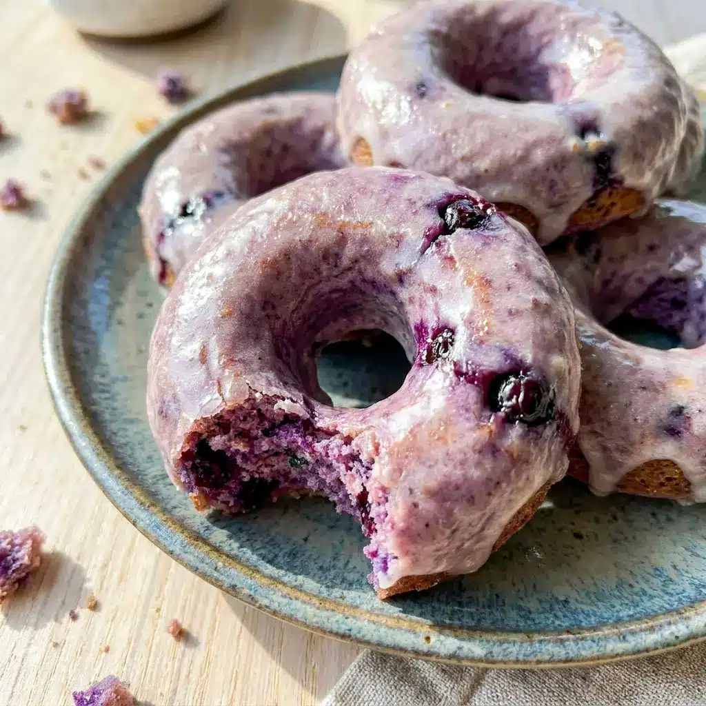 Freshly glazed Blueberry Cake Donuts stacked on a cooling rack with juicy blueberries, perfect for a High Protein Donut Recipe and healthy breakfast treat.